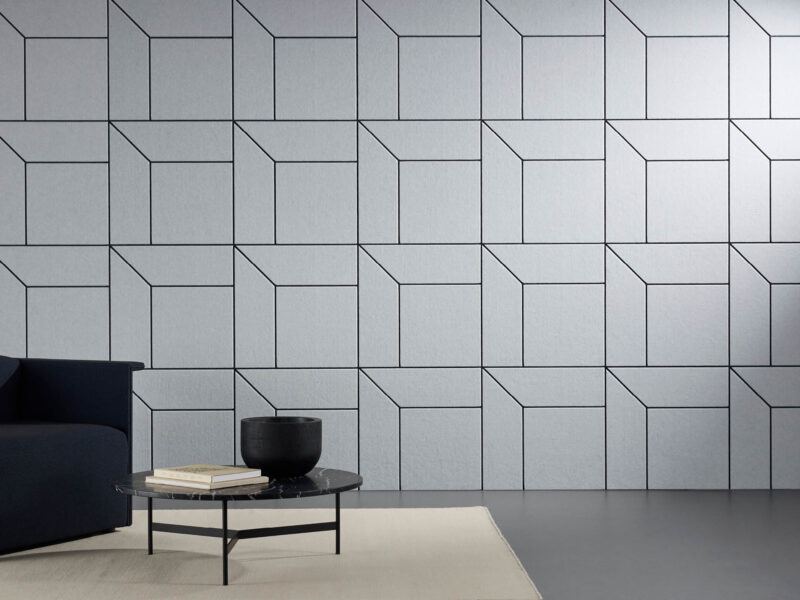 A photo of a room with detailed acoustic panels installed on a wall with an arm chair and coffee table positioned in front